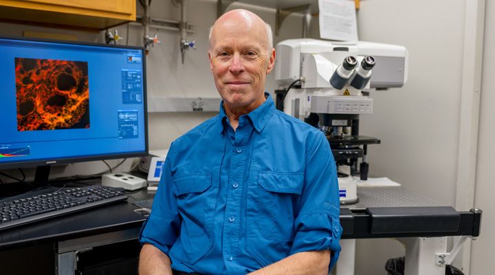 A photo of Steve Ruzin in front of a microscope and computer screen.